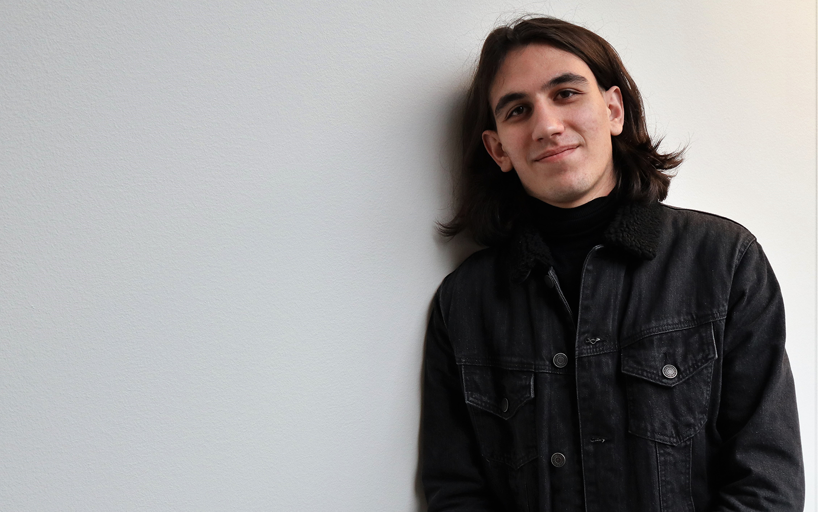 Mihai med halvlangt hår og sort cowboyjakke læner op ad væg