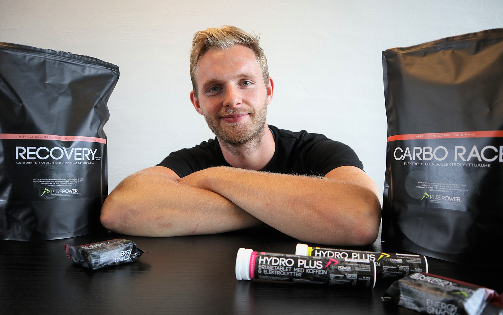 Markedsføringsøkonom Tonias Rasmussen sidder med korslagte arme ved bord fuld af Pure Power-produkter omkring sig