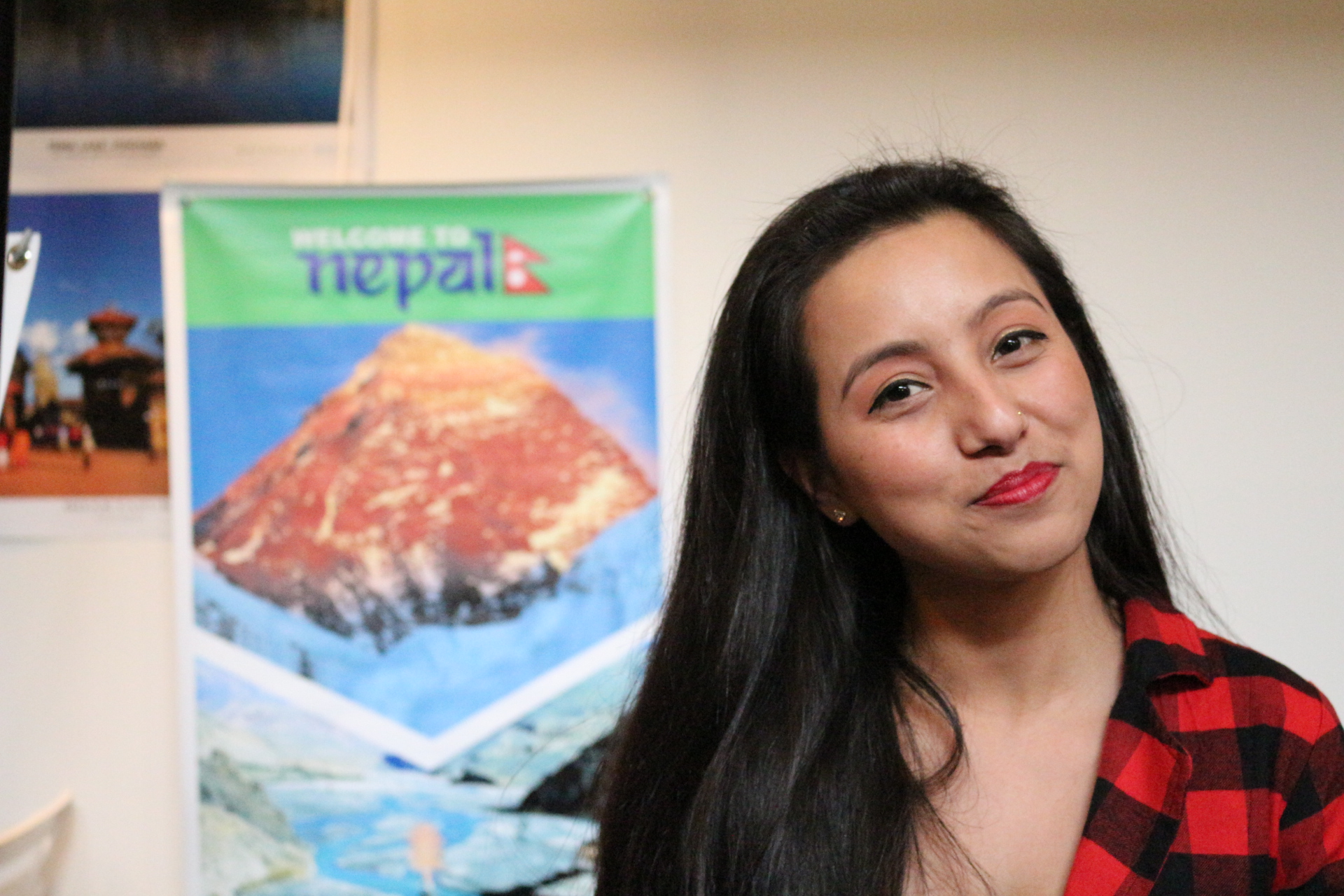 Student smiling in front of poster about Nepal