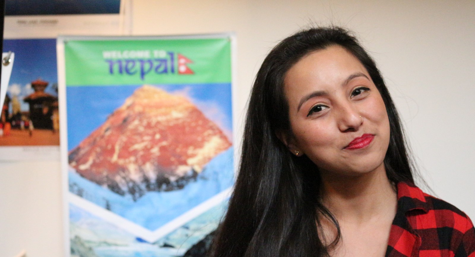 Student smiling in front of poster about Nepal