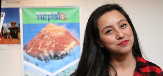 Student smiling in front of poster about Nepal